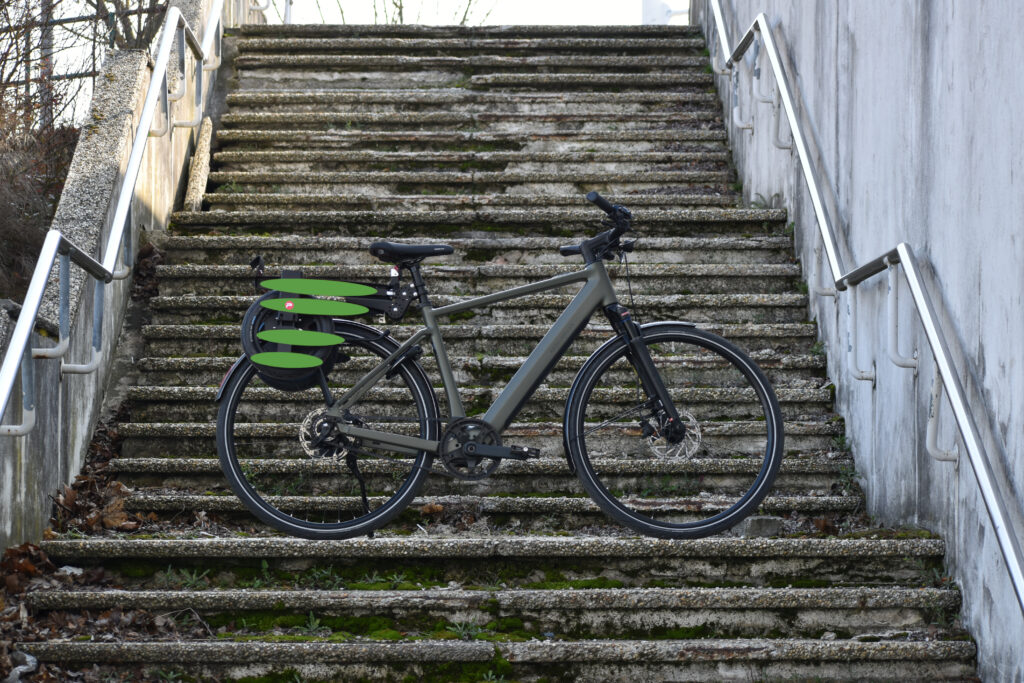 Riese & Müller Pedelec Fahrrad auf Treppenaufgang mit grünem Pullit Fahrradanhänger.