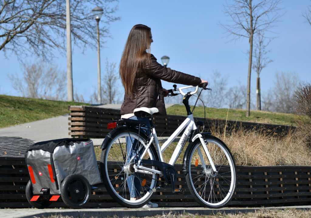 Junge Frau mit Pullit Fahrradanhänger und weißem Fahrrad in Parklandschaft.